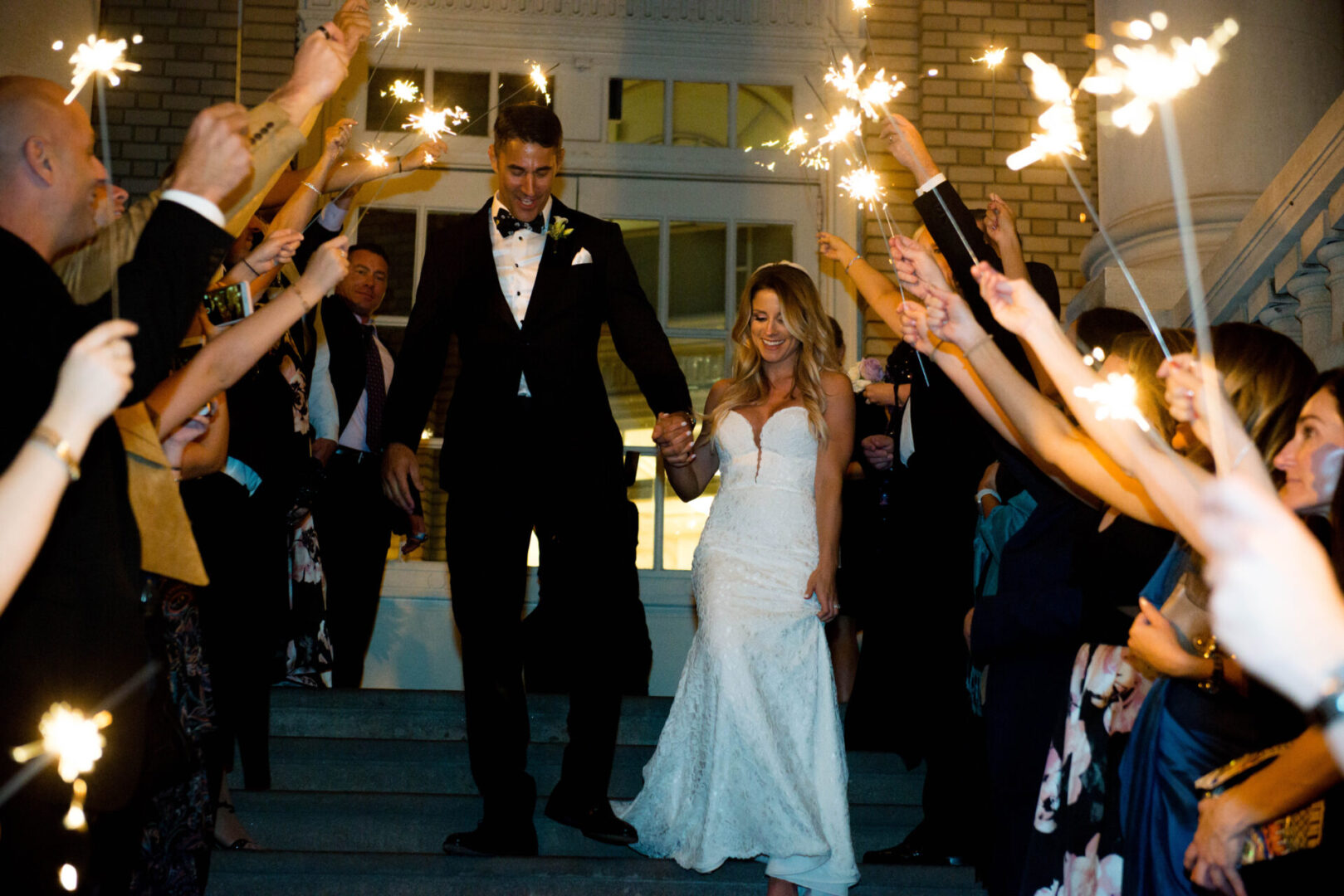 A bride and groom are walking through sparklers.